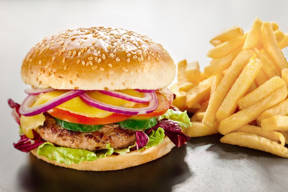 A closeup of a tempting tasty burger with red onion and vegs along with yummy french fries.