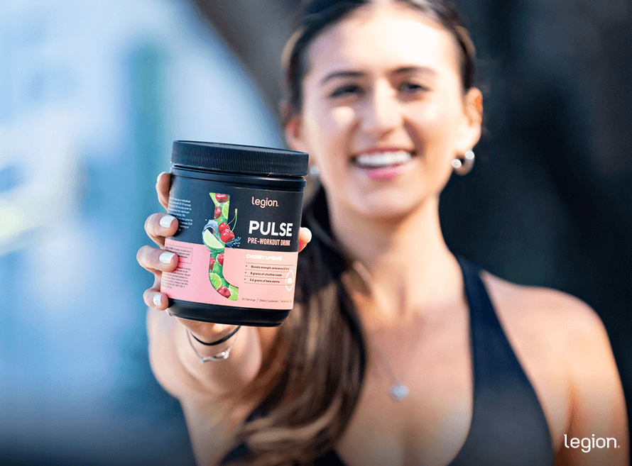 Female smiling while holding pre-workout, illustrating that pre-workout isn't bad for your heart
