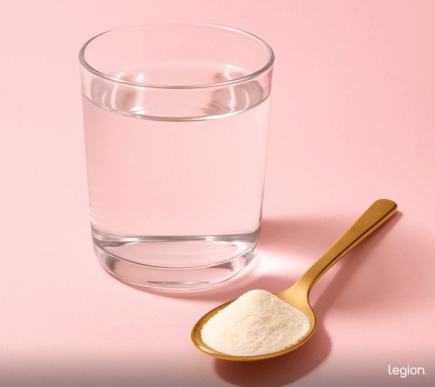 Spoon of collagen protein powder next to a glass of water.