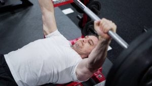 Mike Matthews bench pressing with a barbell to show why barbell bench often allows heavier loads than dumbbell press.