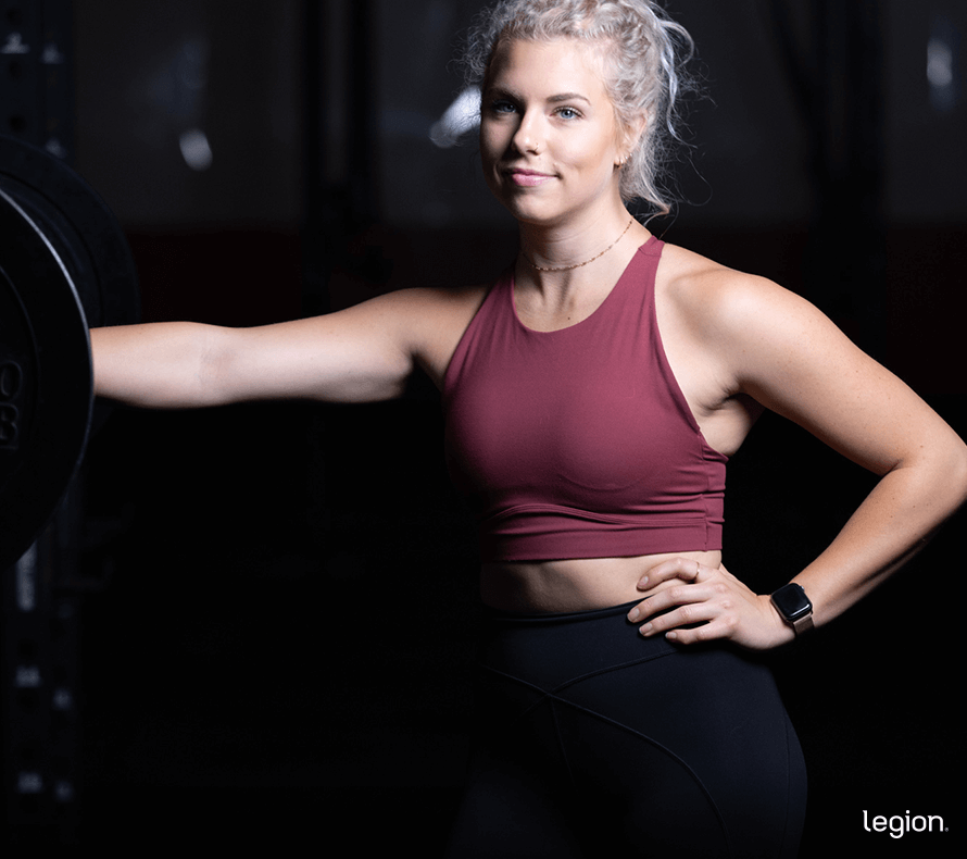 Female athlete standing at a squat rack preparing for a lower-body workout targeting the inner thighs.