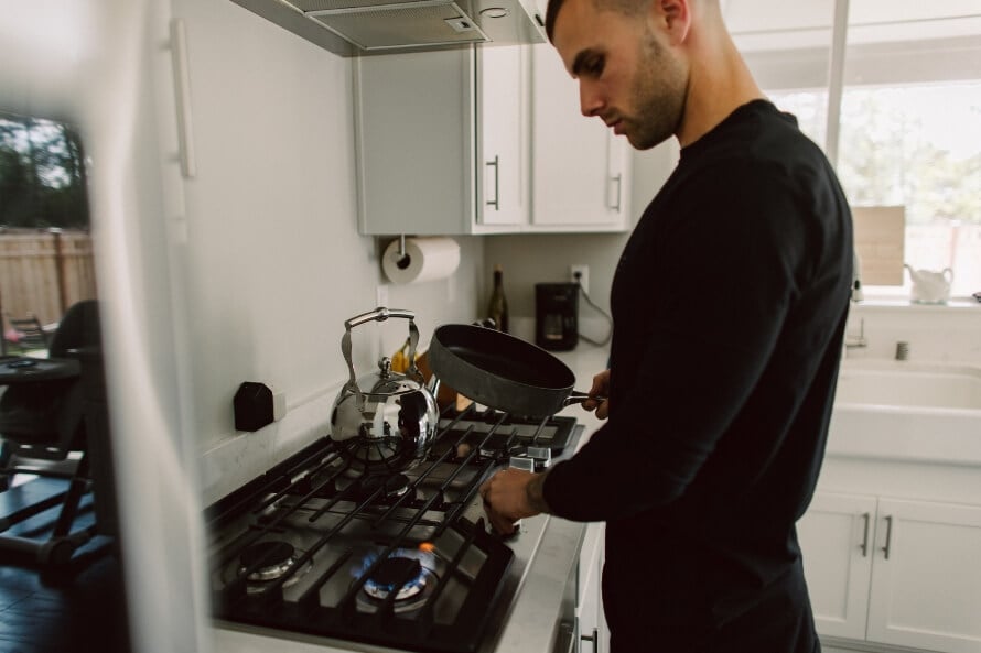 Man in a home kitchen preparing a pre-workout meal, illustrating what to eat and how long to wait to work out after eating. 