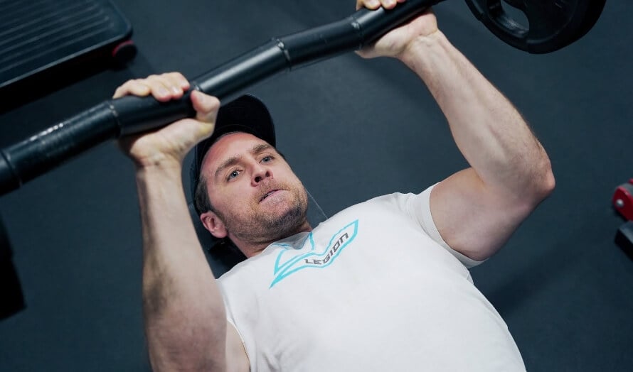 Man performing skullcrushers with an EZ bar to isolate the triceps.