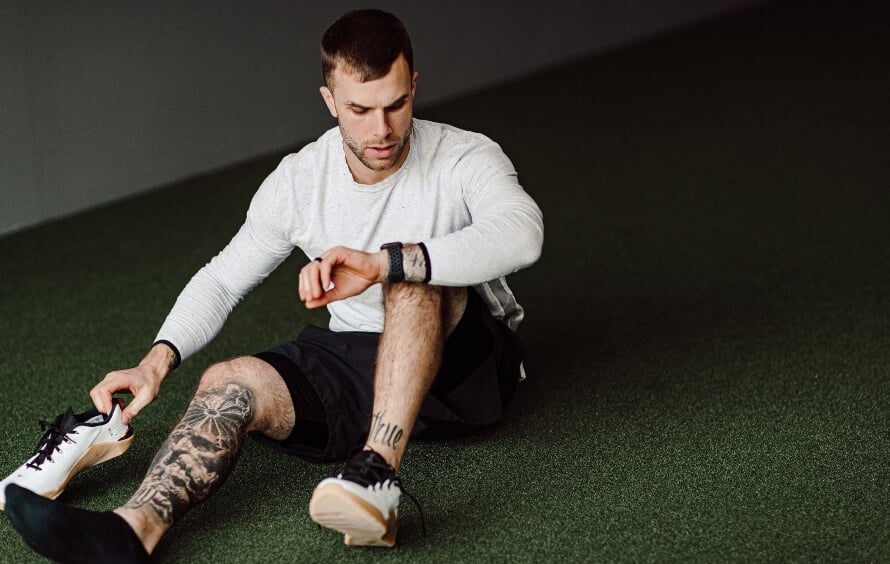 Athlete lacing up training shoes while checking his watch before a workout, showing timing and how long to wait to work out after eating.