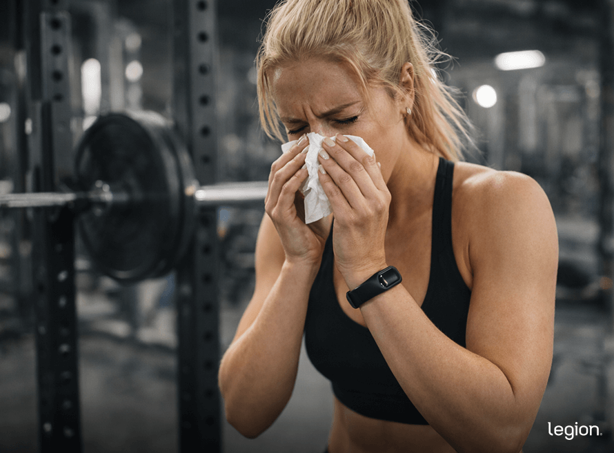 Woman blowing her nose in the gym with a tissue—why you shouldn’t work out when sick if you’re contagious.