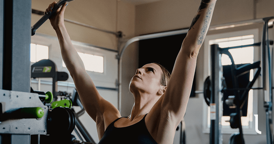 Woman in a black sports bra doing an overhead pull exercise as part of a workout split for women.