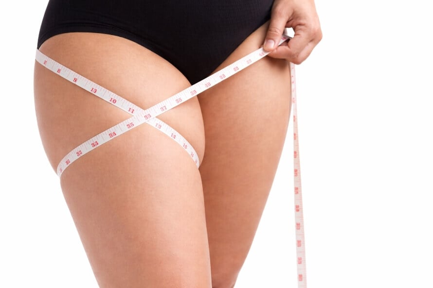 Close-up of a woman measuring outer thigh fat, wondering how to get rid of saddlebags.