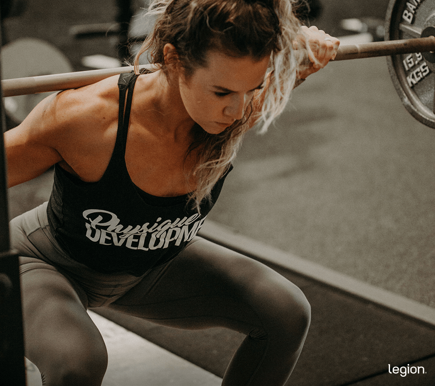 Female athlete in the gym back squatting to build muscle and lose lower back fat.