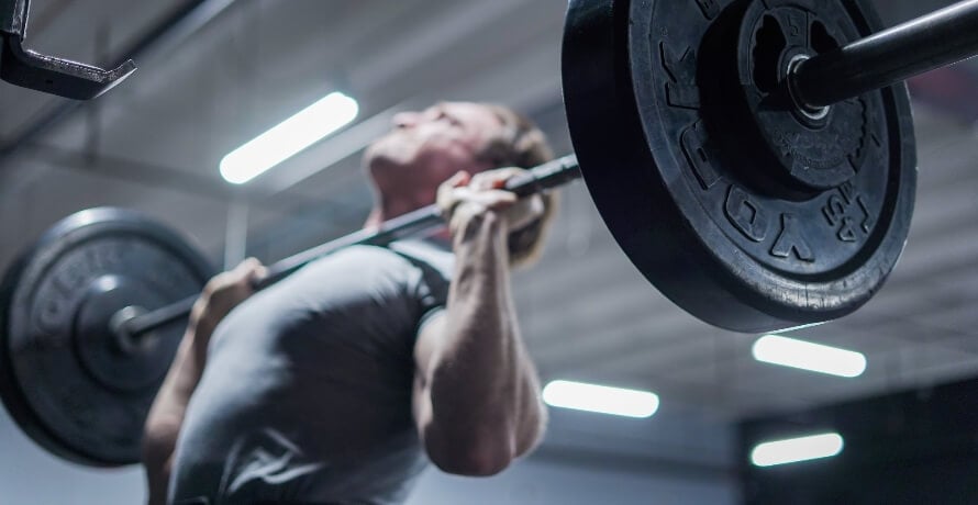 Male athlete performing the barbell overhead press as part of a minimalist workout routine.