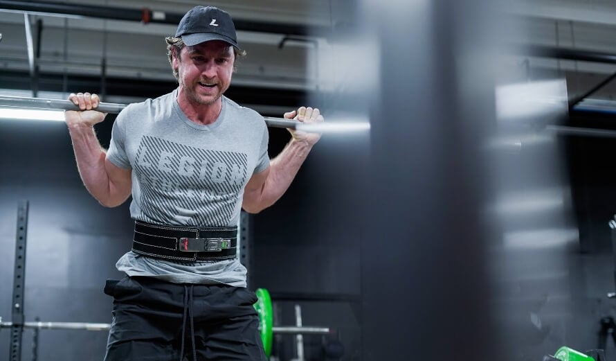 Male athlete back squatting during a 2-day full-body minimalist workout plan.