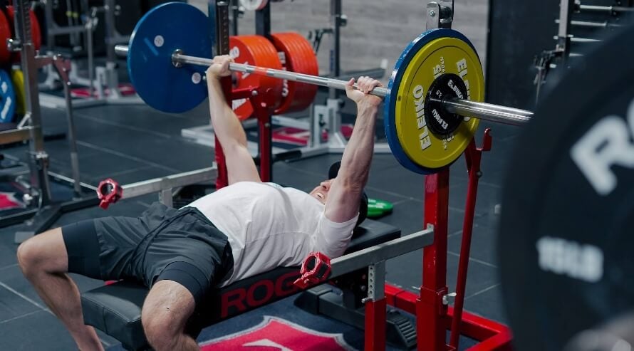 Male athlete in the gym following a minimalist strength training routine that includes the barbell bench press.