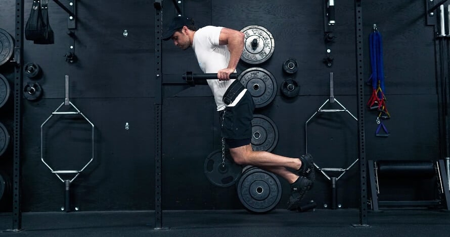 Male athlete doing weighted pull-ups during a minimalist full-body workout.