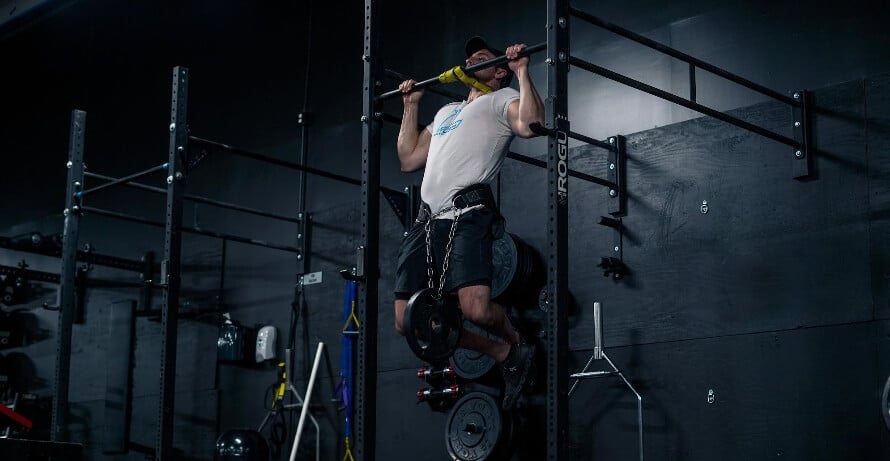 Male athlete doing weighted pull-ups during a minimalist full-body workout.