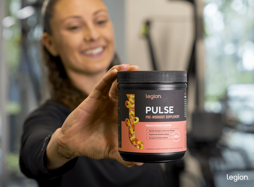 Female athlete holding a tub of pre-workout supplement, getting ready to take it on an empty stomach.