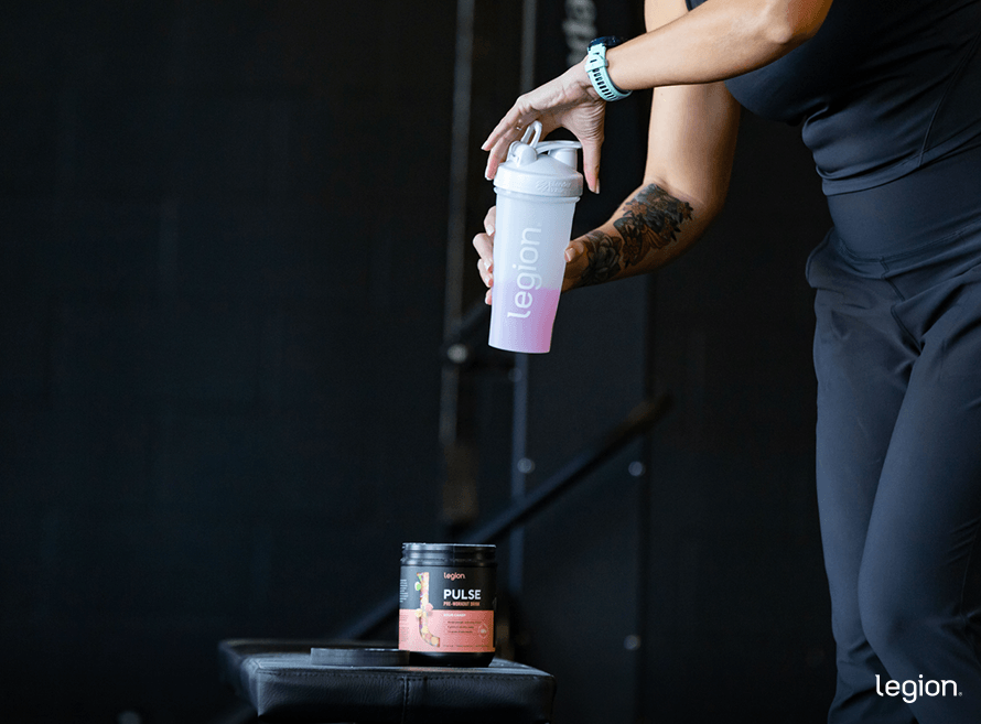 Female athlete preparing pre-workout powder on a gym bench, showing someone considering taking pre-workout without food before a workout.