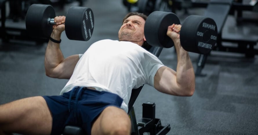 Male athlete doing the incline dumbbell bench press during a chest and back dumbbell workout. 