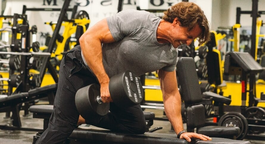 Male athlete doing one-arm dumbbell rows as part of a chest and back workout with supersets.