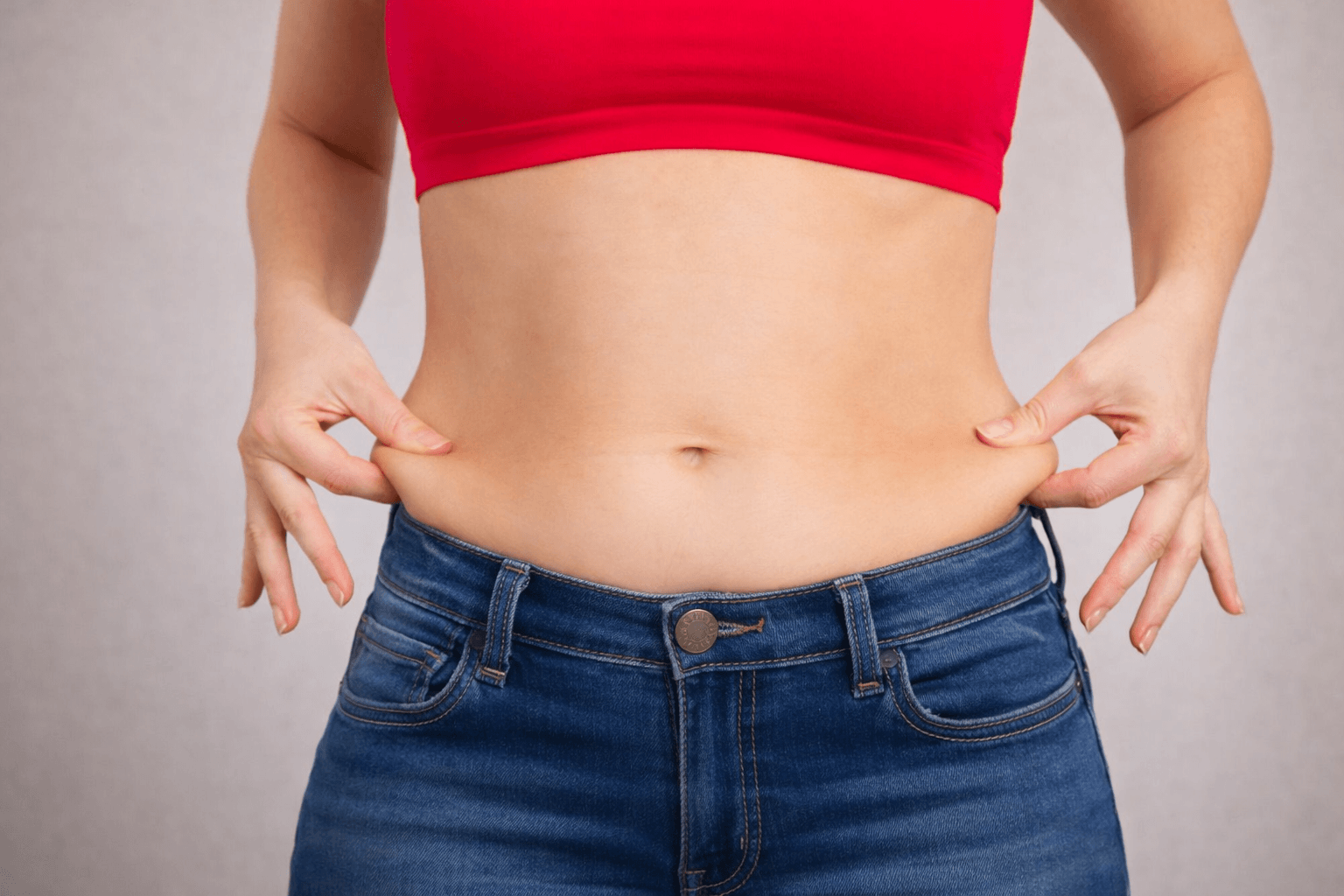 Image of a women pinching her muffin top fat that sits above her waistband.