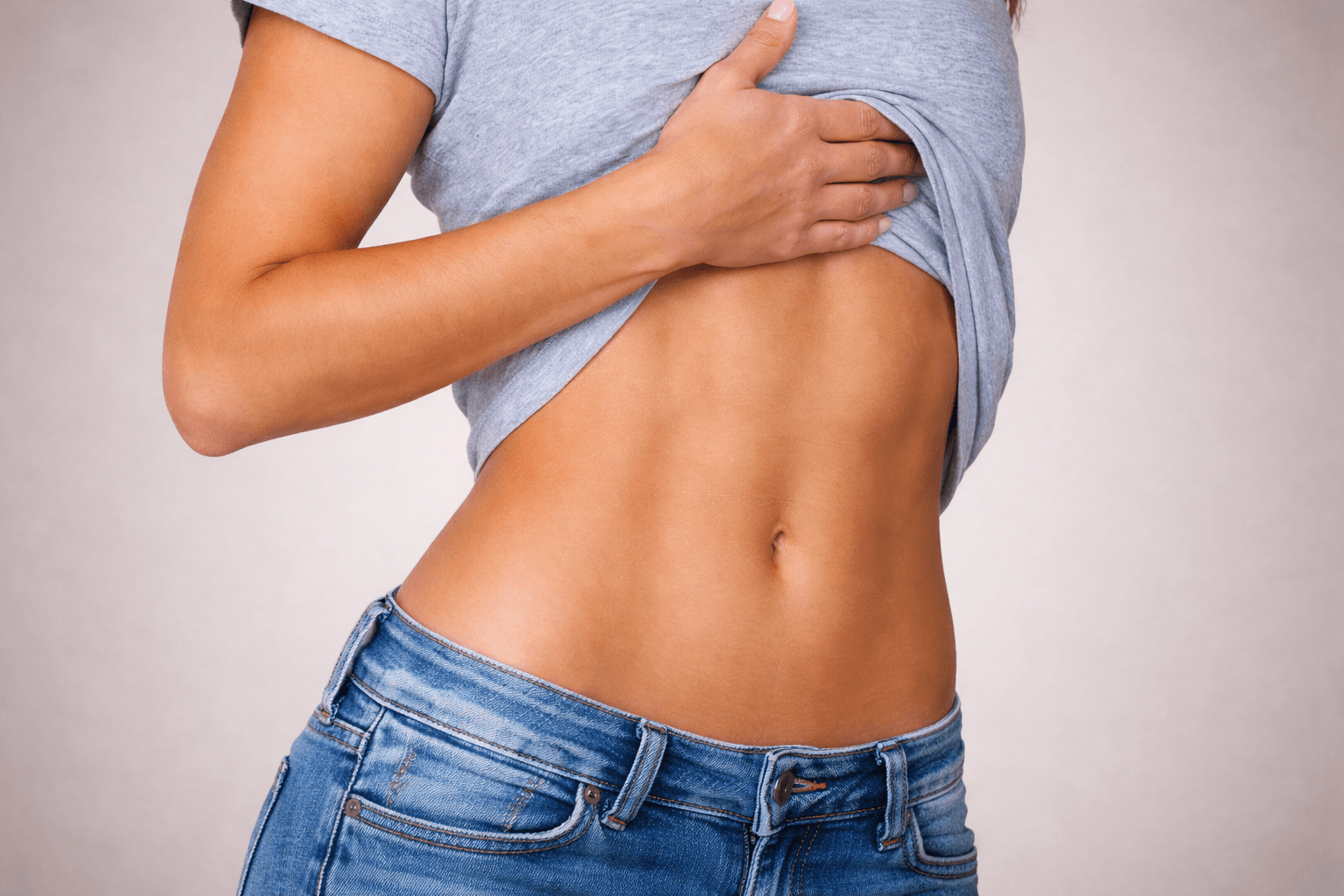 Athletic women wearing jeans showing how abs look once you get rid of a muffin top.