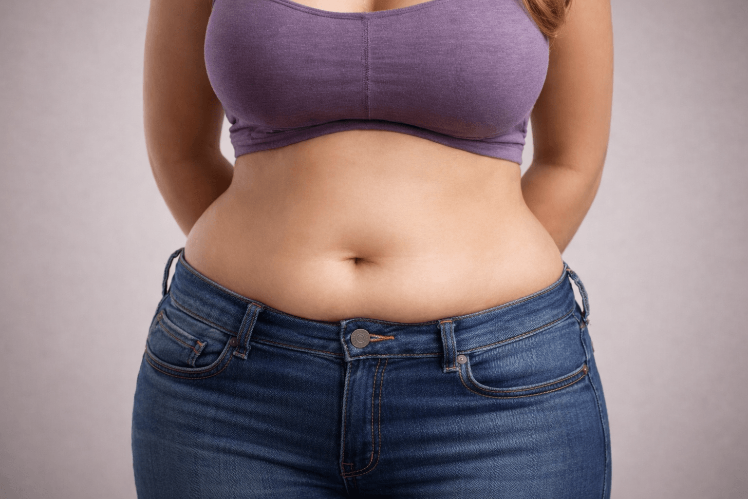 Image of women from the front showing slightl muffin top above the waistband of her jeans.