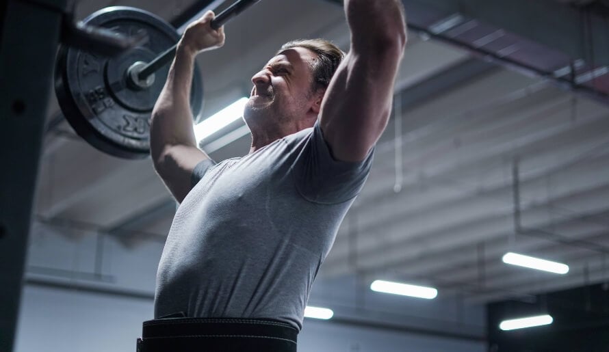 Male athlete in the gym performing the overhead press as part of a push pull legs upper lower split.