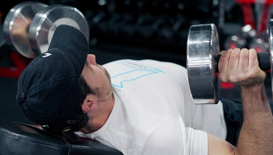 Male athlete doing dumbbellincline bench press during a 3-day full-body dumbbell workout.