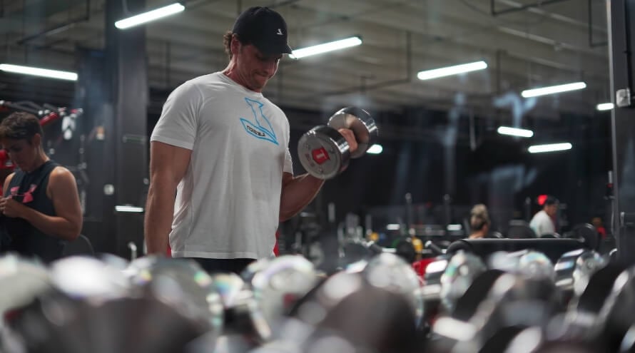 Male athlete doing dumbbell biceps curls as part of a full-body dumbbell workout plan. 