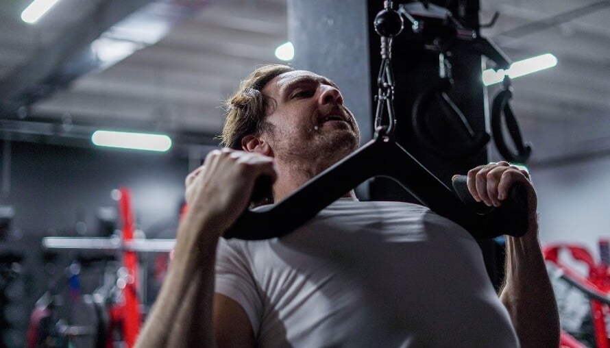 Male athlete performing the lat pulldown in the gym as part of a back and triceps workout routine.