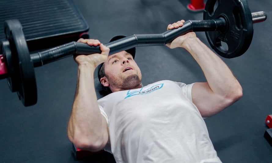 Male athlete performing the skullcrusher, an excellent exercise to include in a back and triceps workout routine.