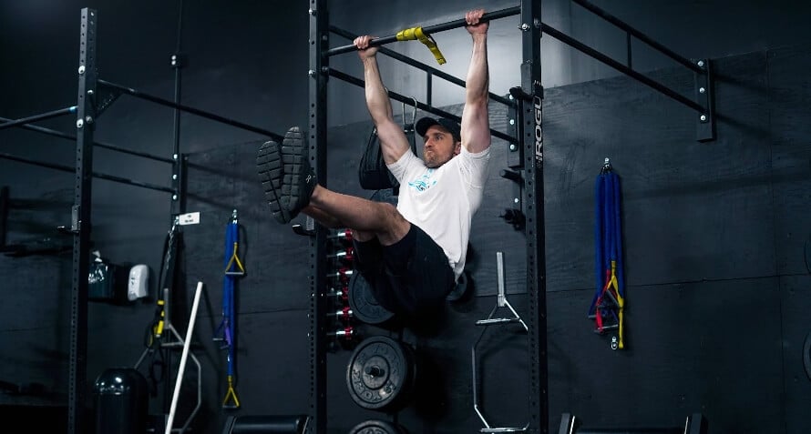 Male athlete doing hanging leg raises in the gym as part of a lower ab workout.