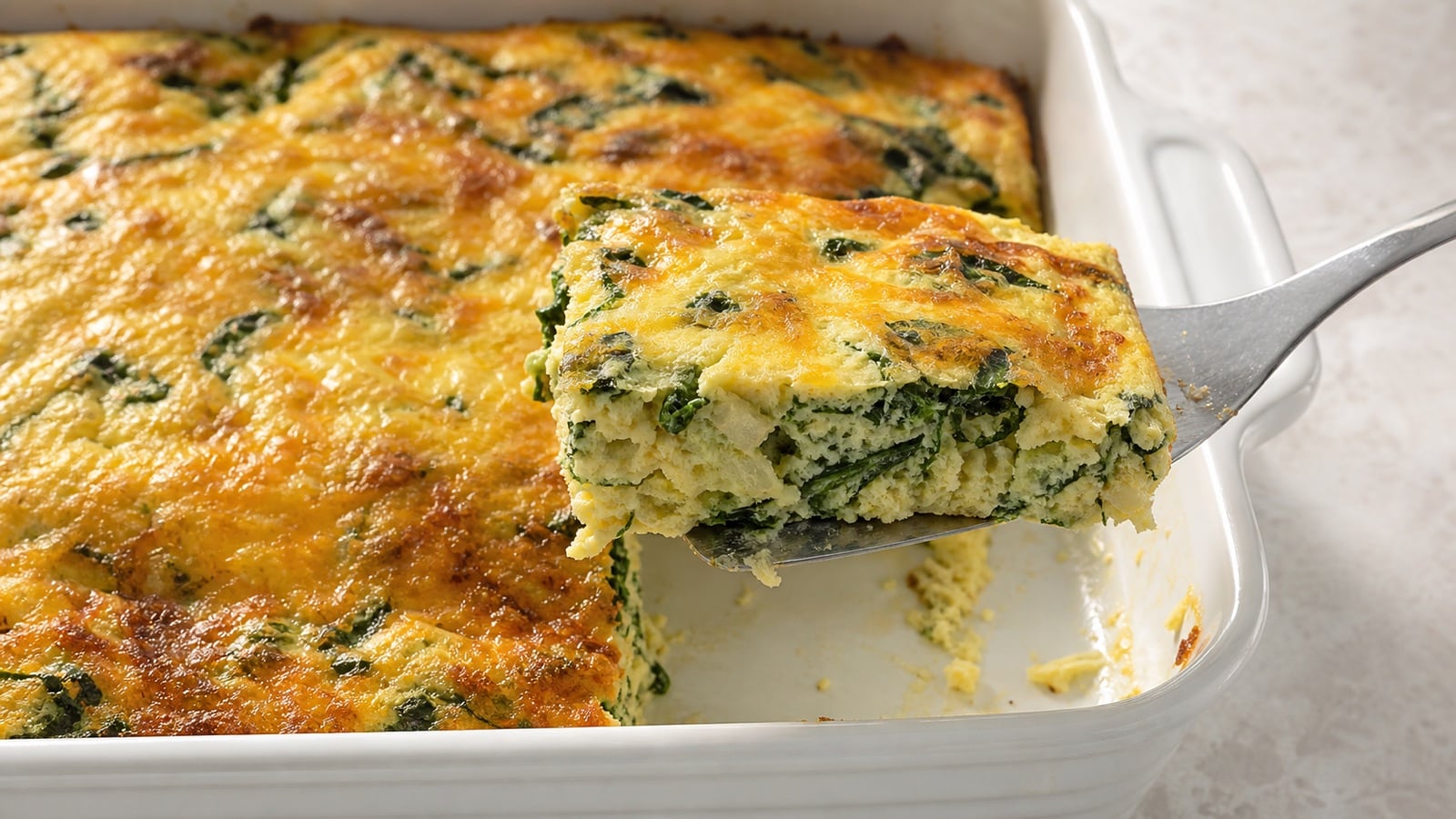 Close spinach cheese casserole with a tender interior and a serving lifted from the baking dish