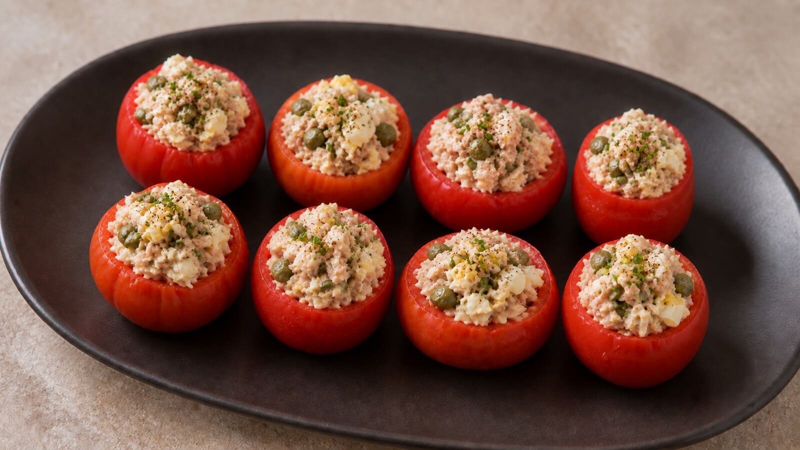 Eight tuna-stuffed Campari tomatoes on a dark plate